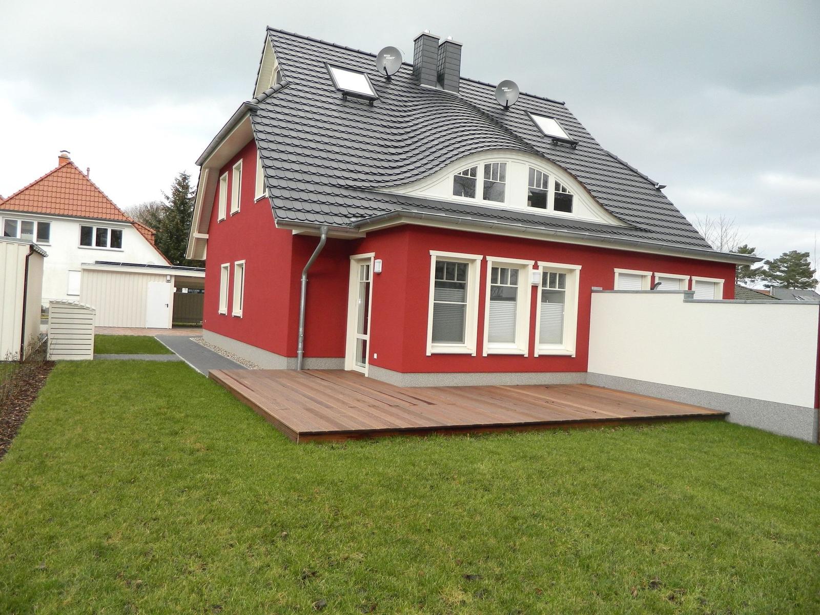 Rotes Haus mit Dachterrasse und Holzterrasse im Garten.