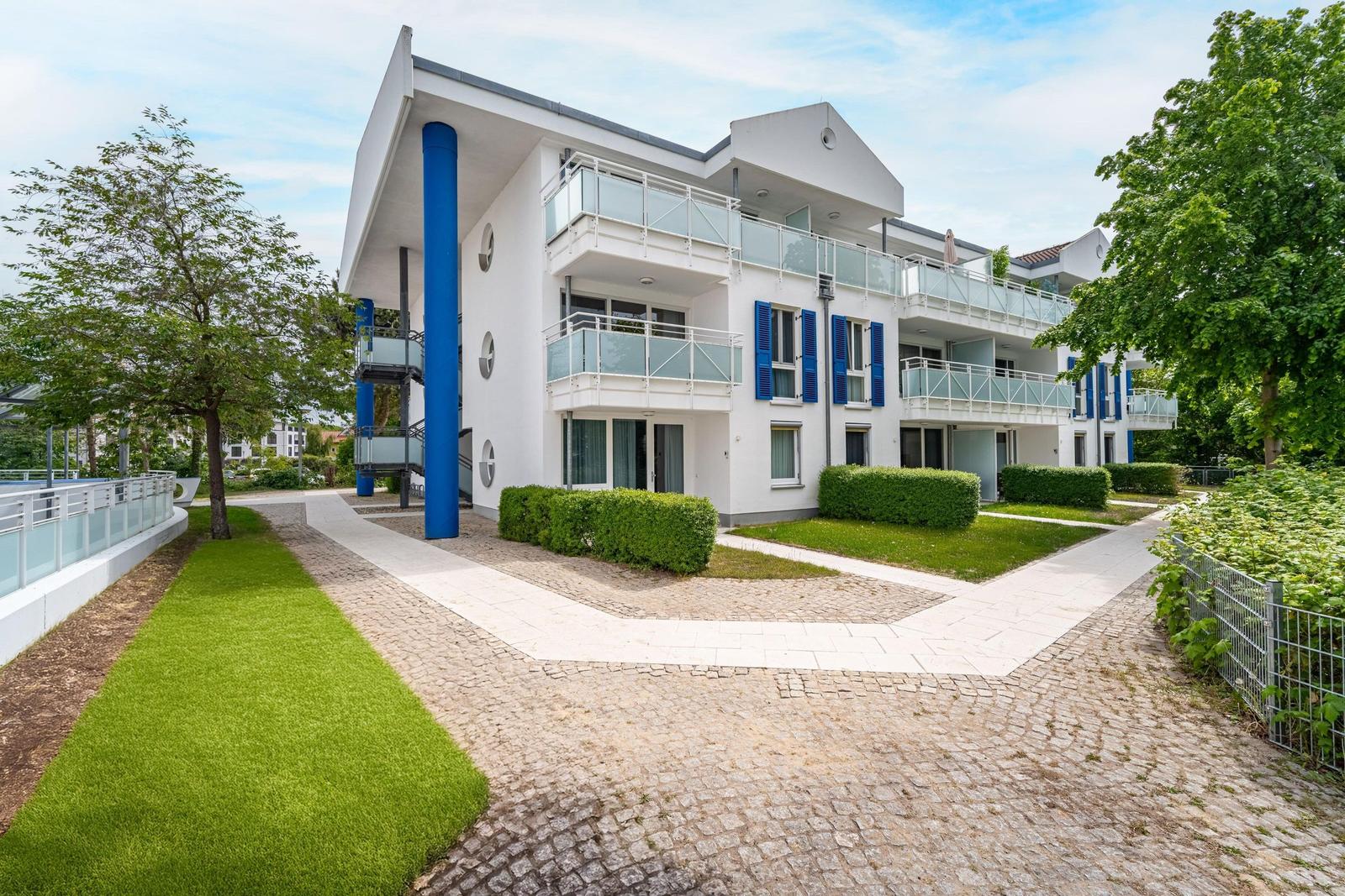 Grüner Rasen mit Blumen, Pfad und Bäume vor einem Wohnhaus.