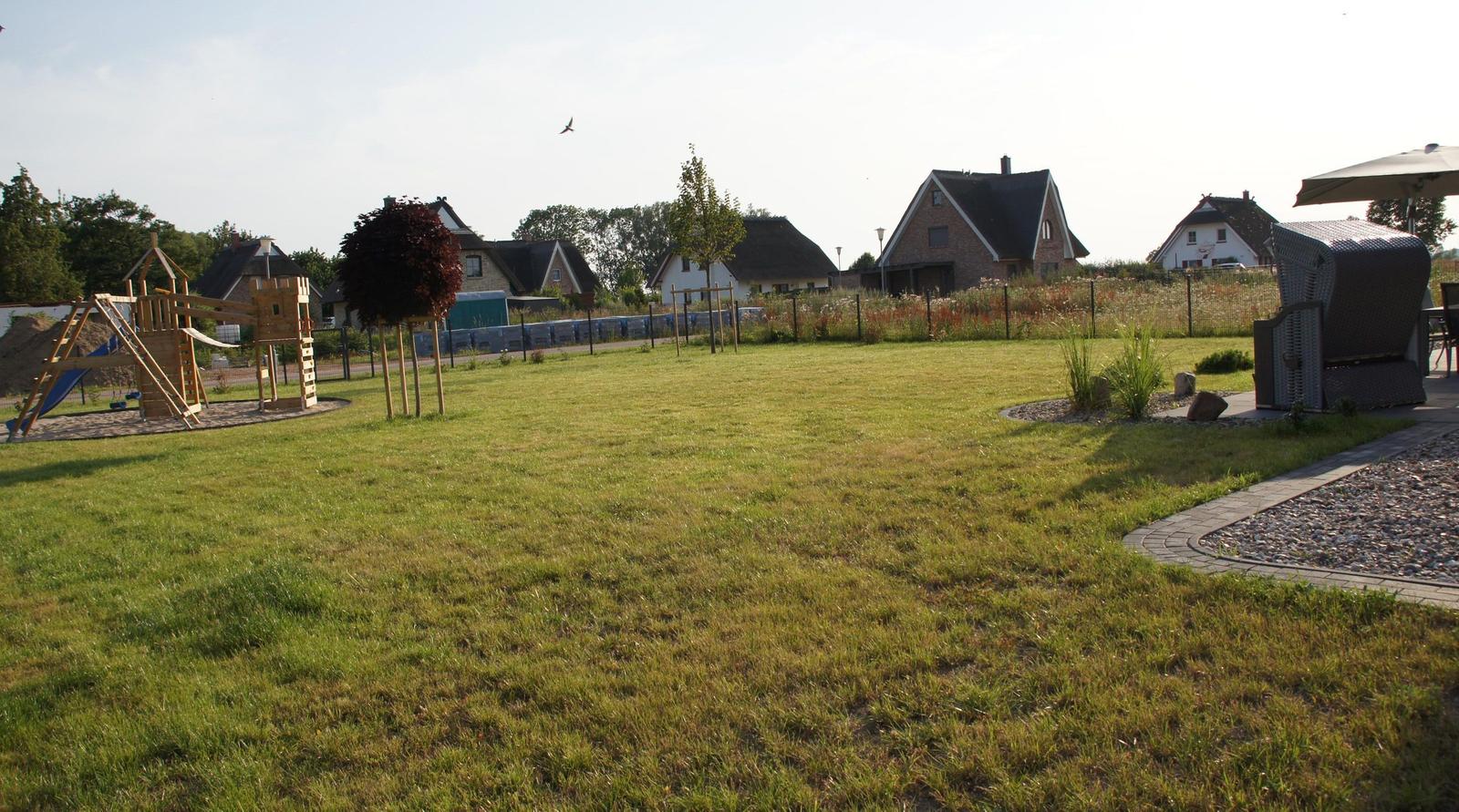 Strand mit Gras im Vordergrund und Meer im Hintergrund unter blauem Himmel.