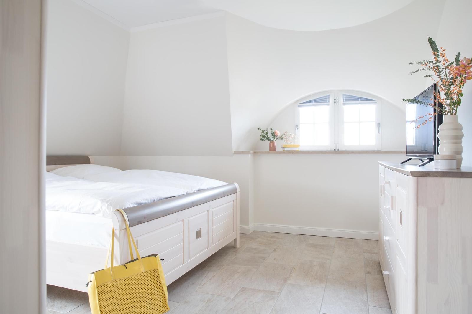 Schlafzimmer mit Bett, TV und Fenster unter Dachschrägen.