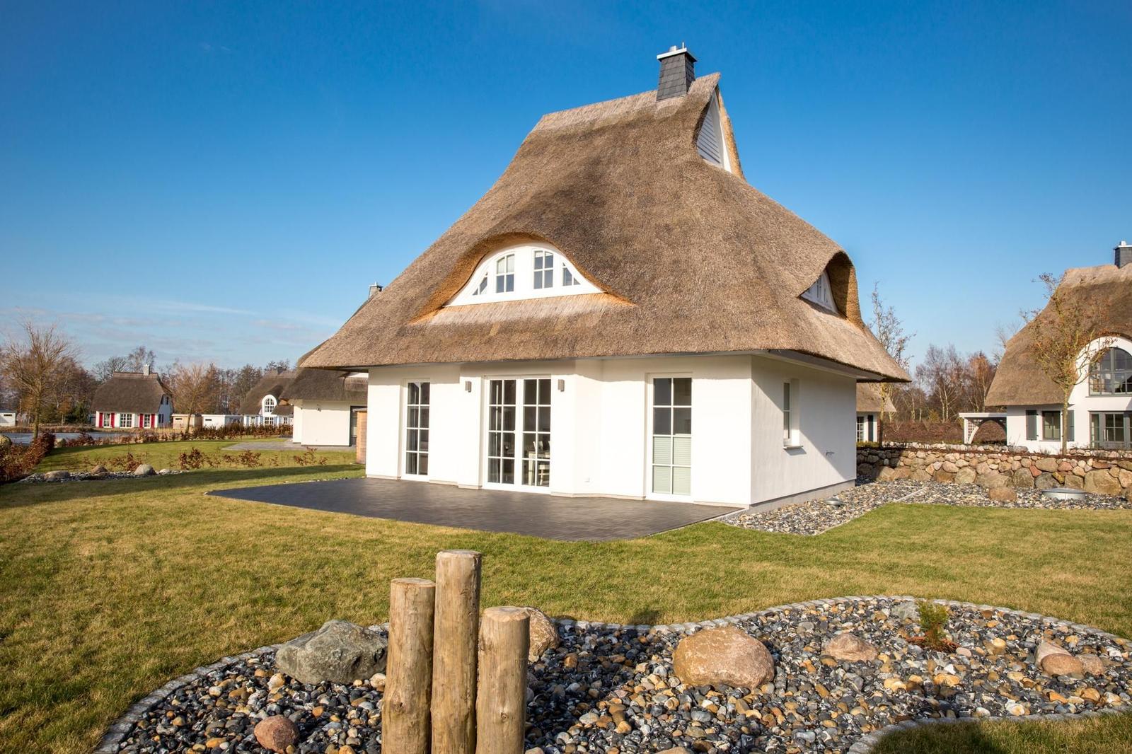 Haus mit strohgedecktem Dach und weißen Wänden. Vorhof mit Steinplatten und Rasen.