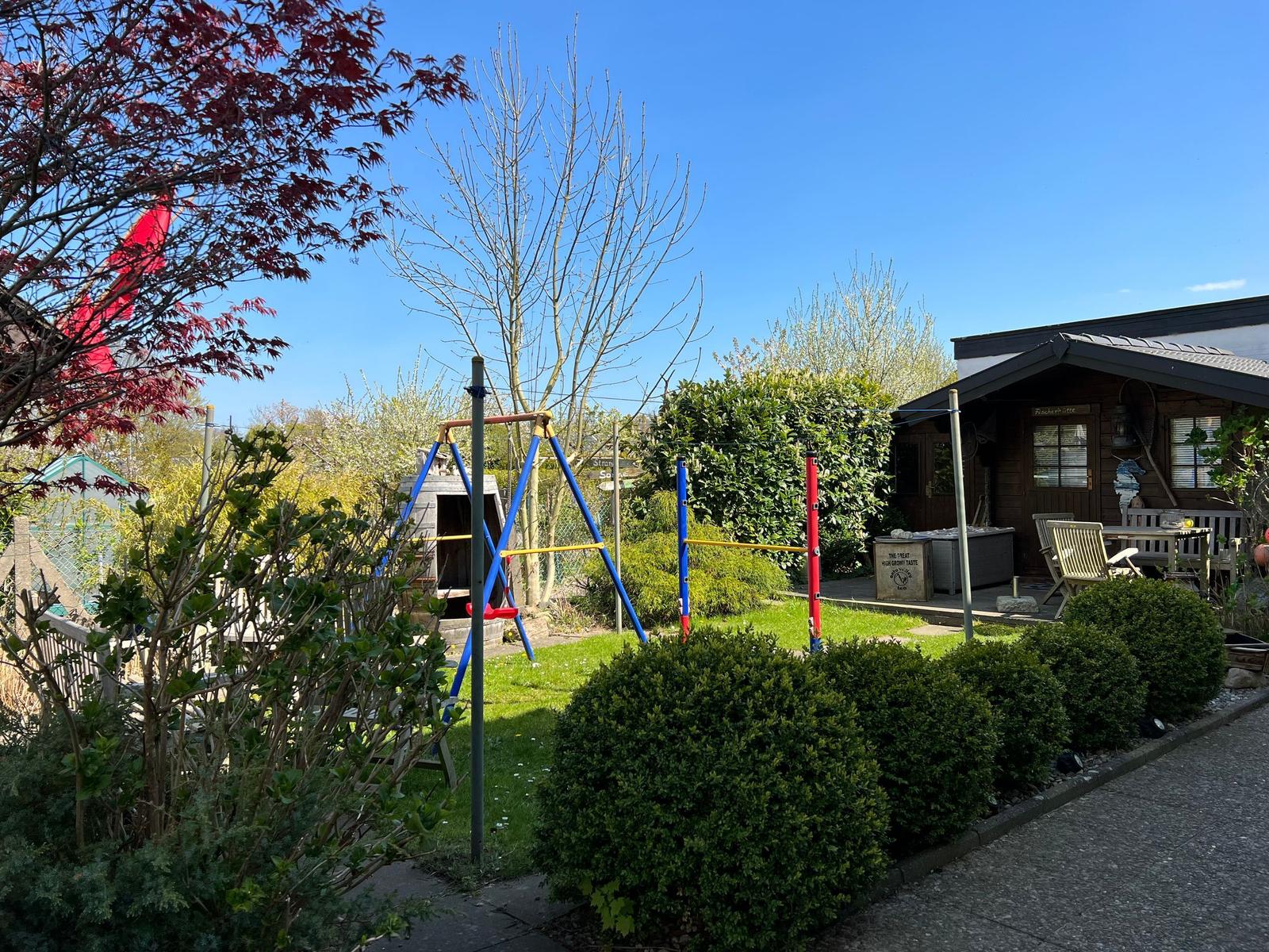 Terrasse mit Holztisch, Stühlen und Garten. Hinterhof mit Hecke und Dekoration.