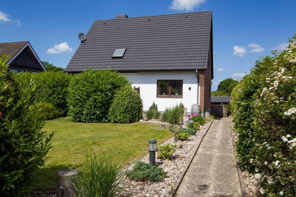 Haus mit Garten, Spielplatz und Terrasse unter blauem Himmel.