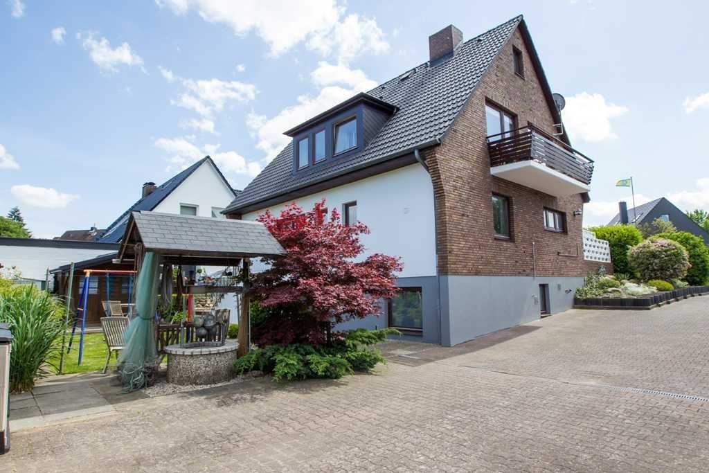 Ein zweistöckiges Haus mit Balkon, Garten und Terrasse unter blauem Himmel.