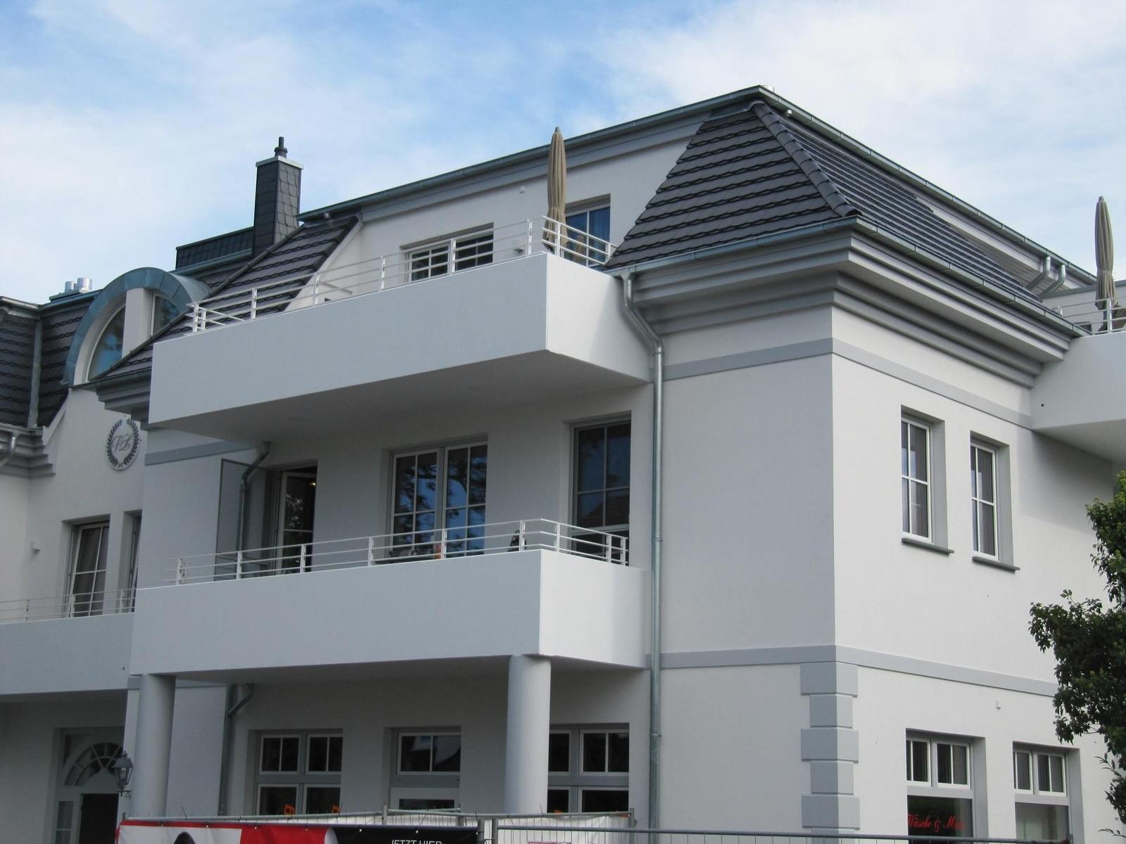 Modern white building with balconies and dormer windows under a blue sky.