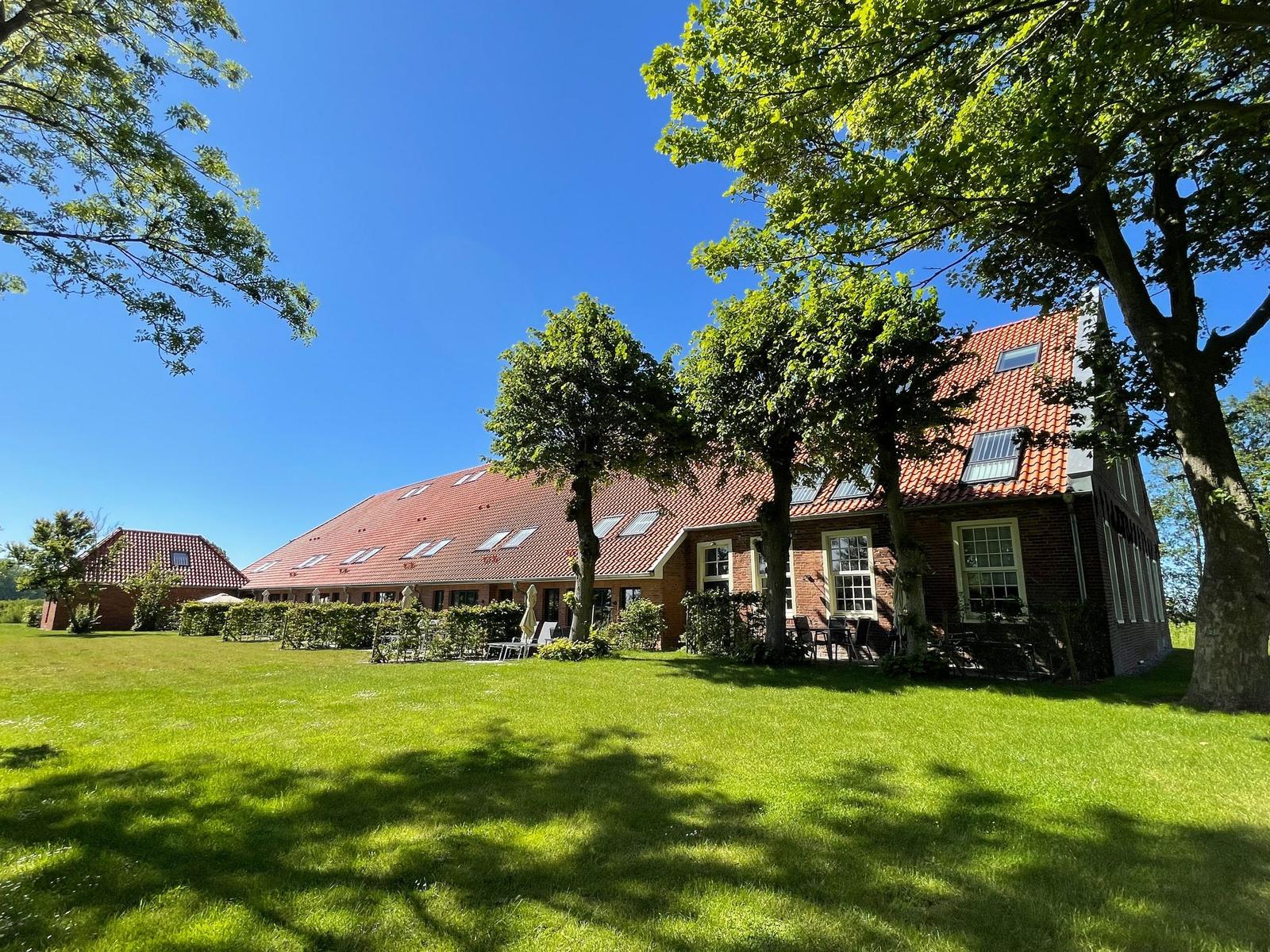 Terrasse mit Tisch, Stühlen und Grill. Blick auf grüne Wiesen und Bäume unter blauem Himmel.