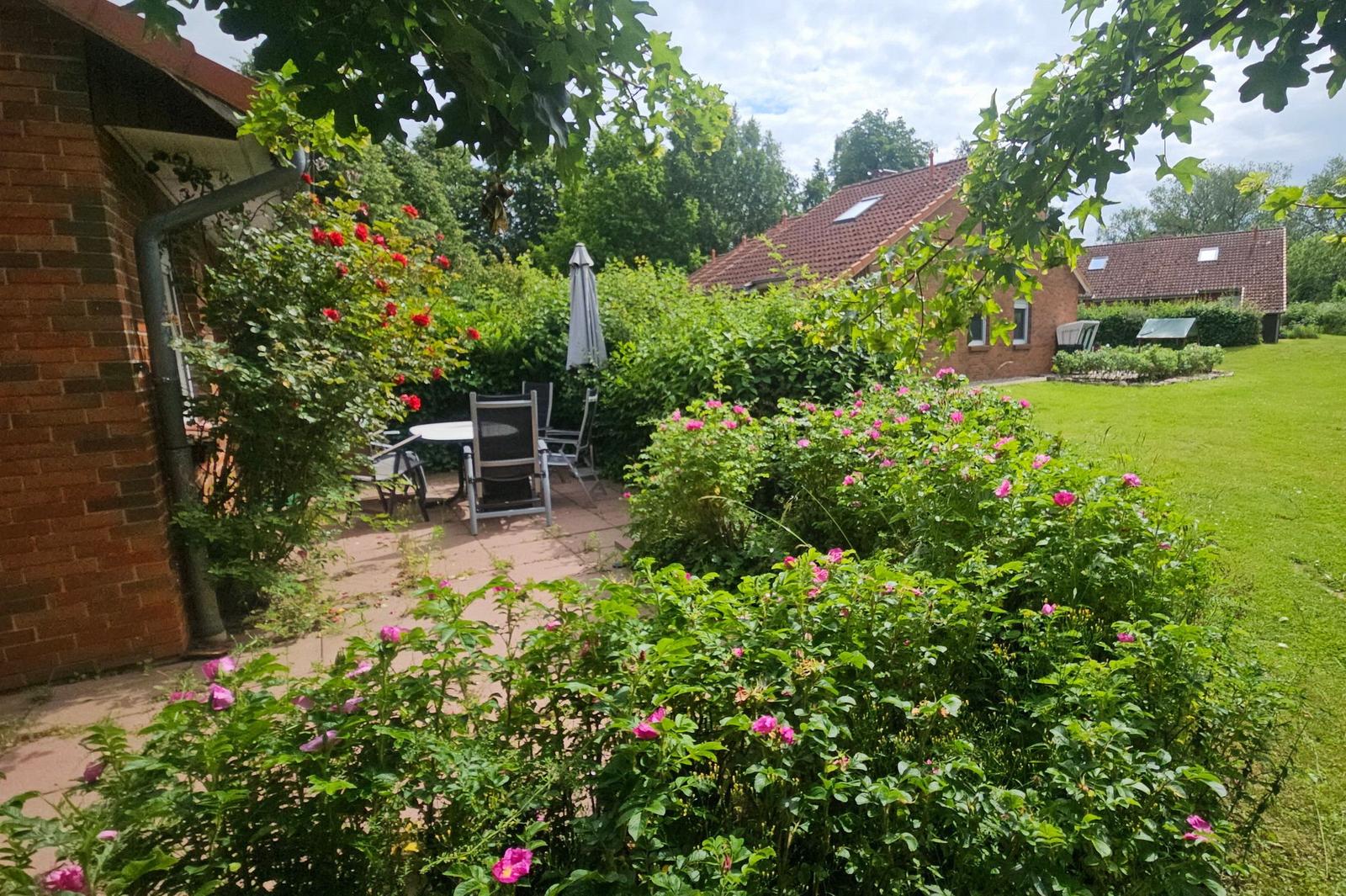 Hinterhof mit Terrasse, Blumenbeeten und Gartenhaus. Roter Ziegelbau mit Schornstein.