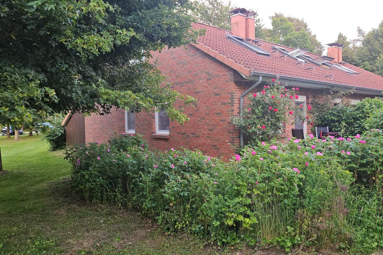 Rotes Ziegelhaus mit Garten, Rosen und Bäumen. Dach mit Solaranlagen.