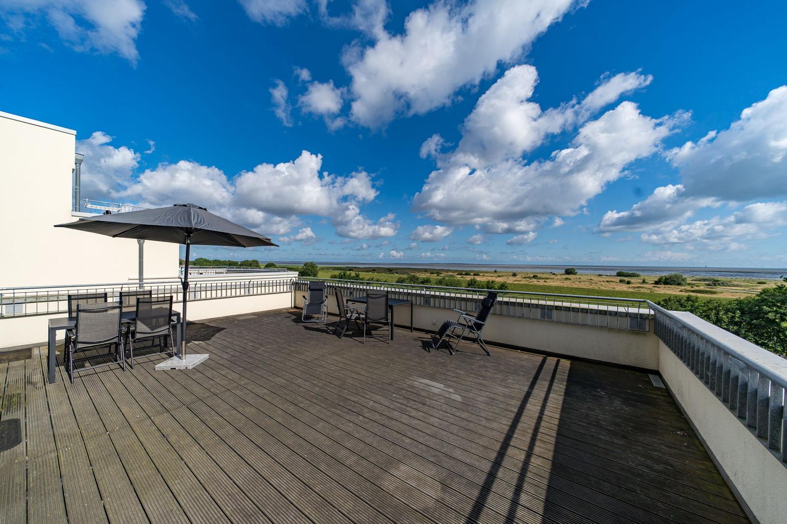 Weitläufiger Blick auf Fluss, Grünflächen und Horizont unter blauem Himmel mit weißen Wolken.