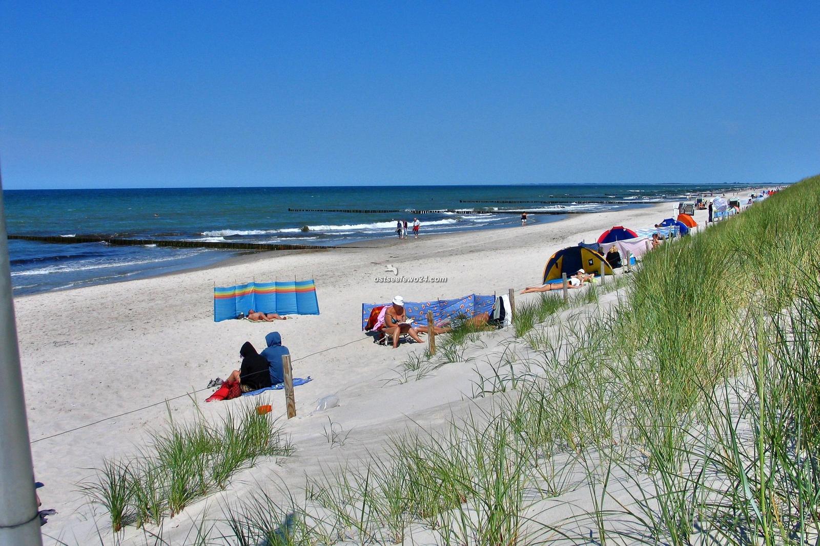 Strand mit Strandkörben, Spielplatz und Badegästen unter blauem Himmel.