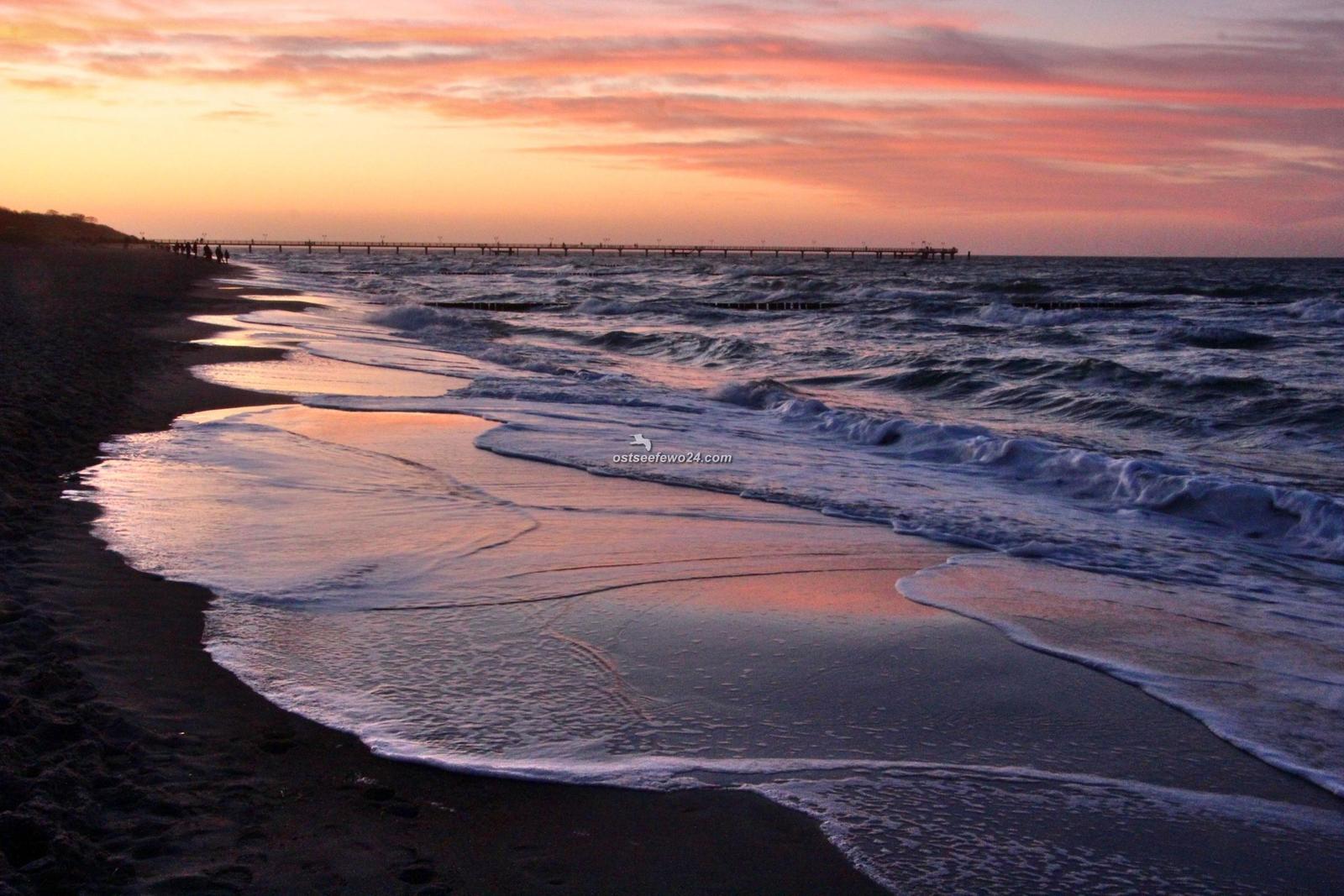 Strand mit weißen Sand, Wellen und Sonnenschirmen. Menschen entspannen sich am Ufer.