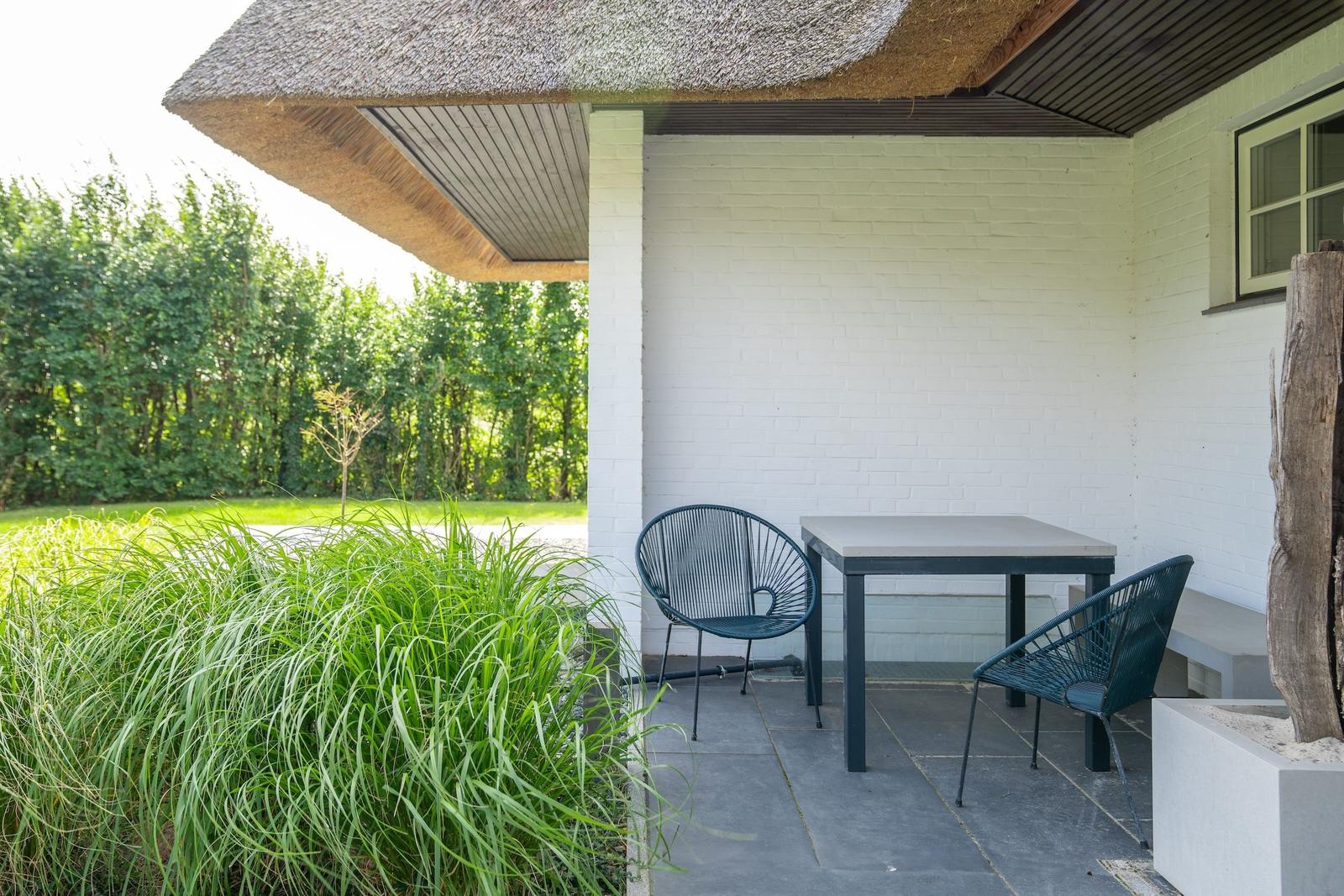 Patio with table and two chairs under thatched eaves.