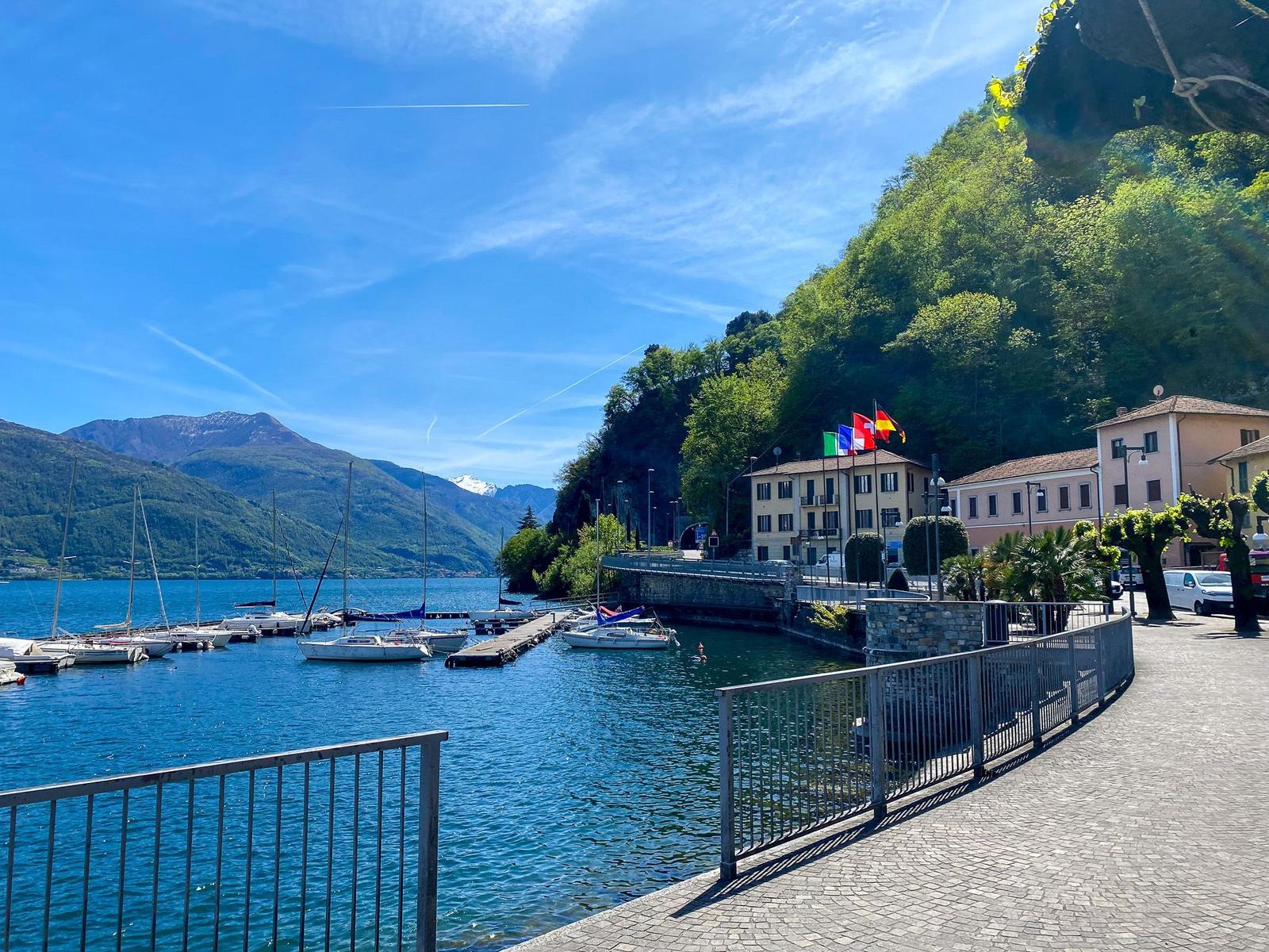 Lakeside town with colorful buildings, boats on water, and mountains in background.