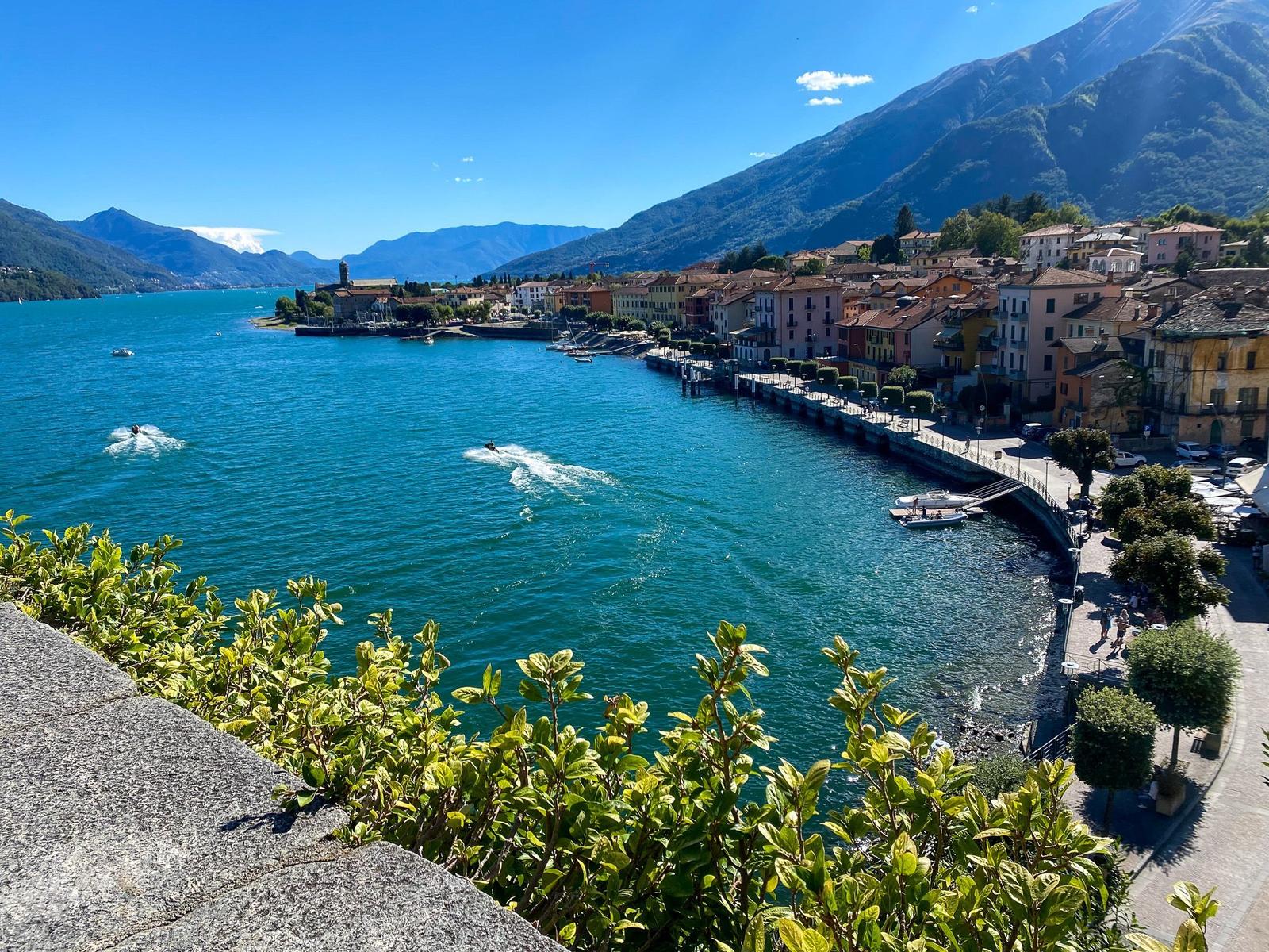 Außenbereich mit grünen Sonnenschirmen und roten Stühlen am Wasser.