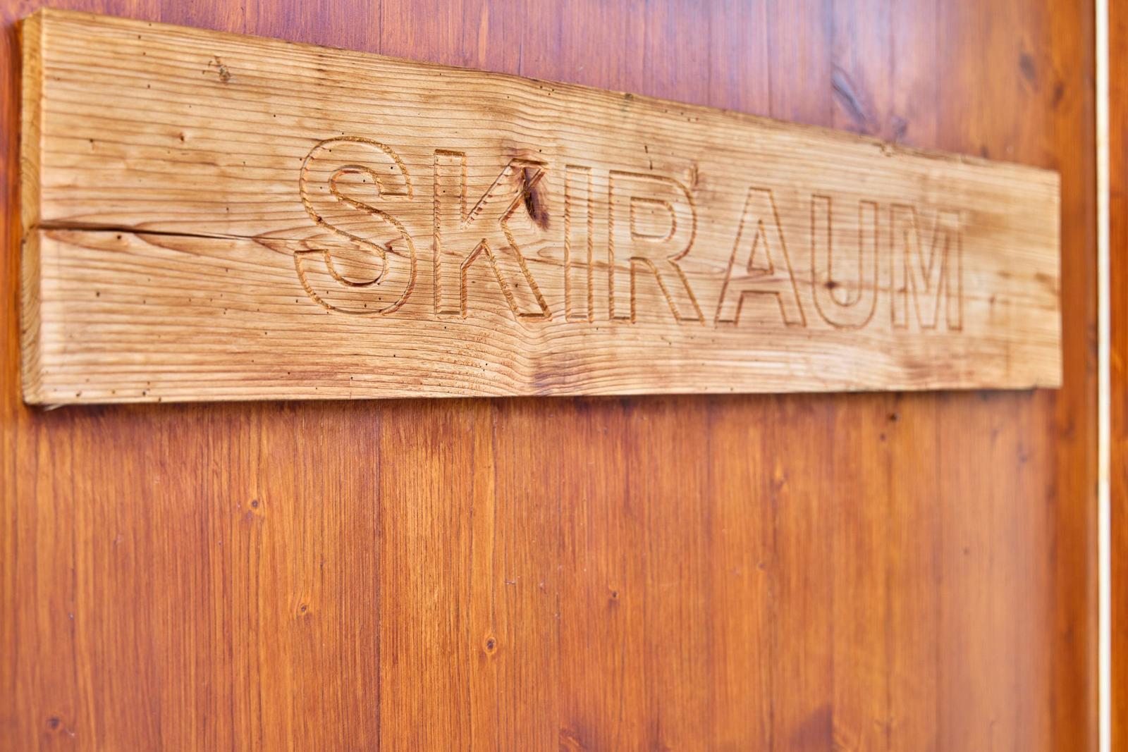 Skiraum mit Holzbank, Felldecke und Wandregal. Holztür mit Skiraum-Schild.