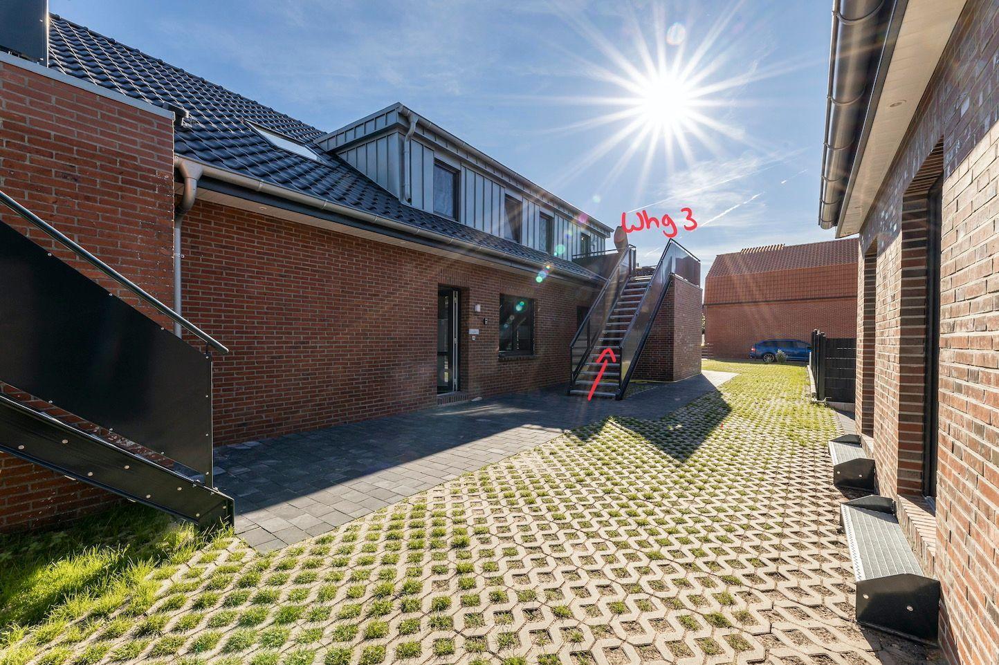 Two bicycles stand under a roof next to a brick wall on paving stones.