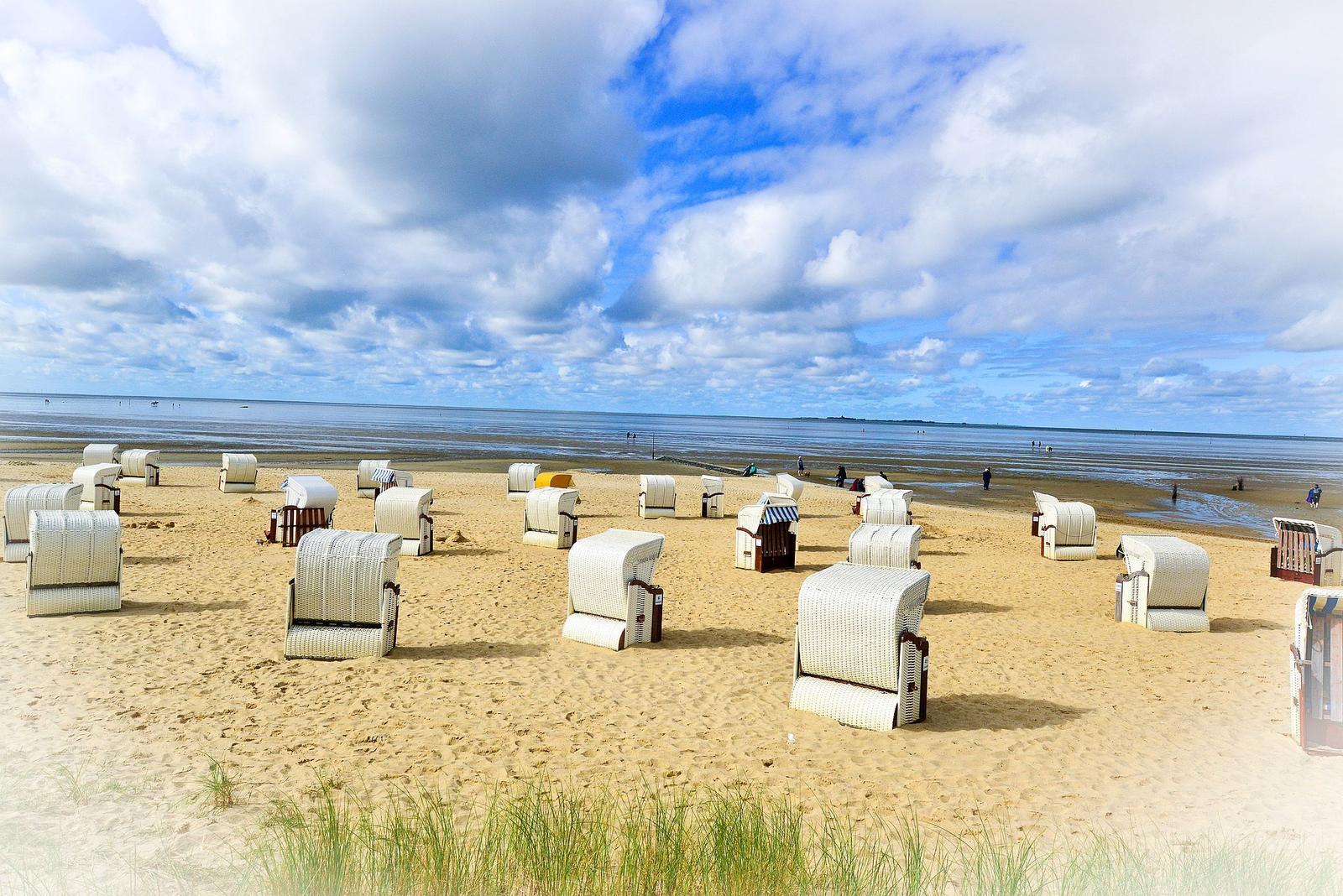 Strand mit Strandkörben und Blick auf das Meer unter bewölktem Himmel.