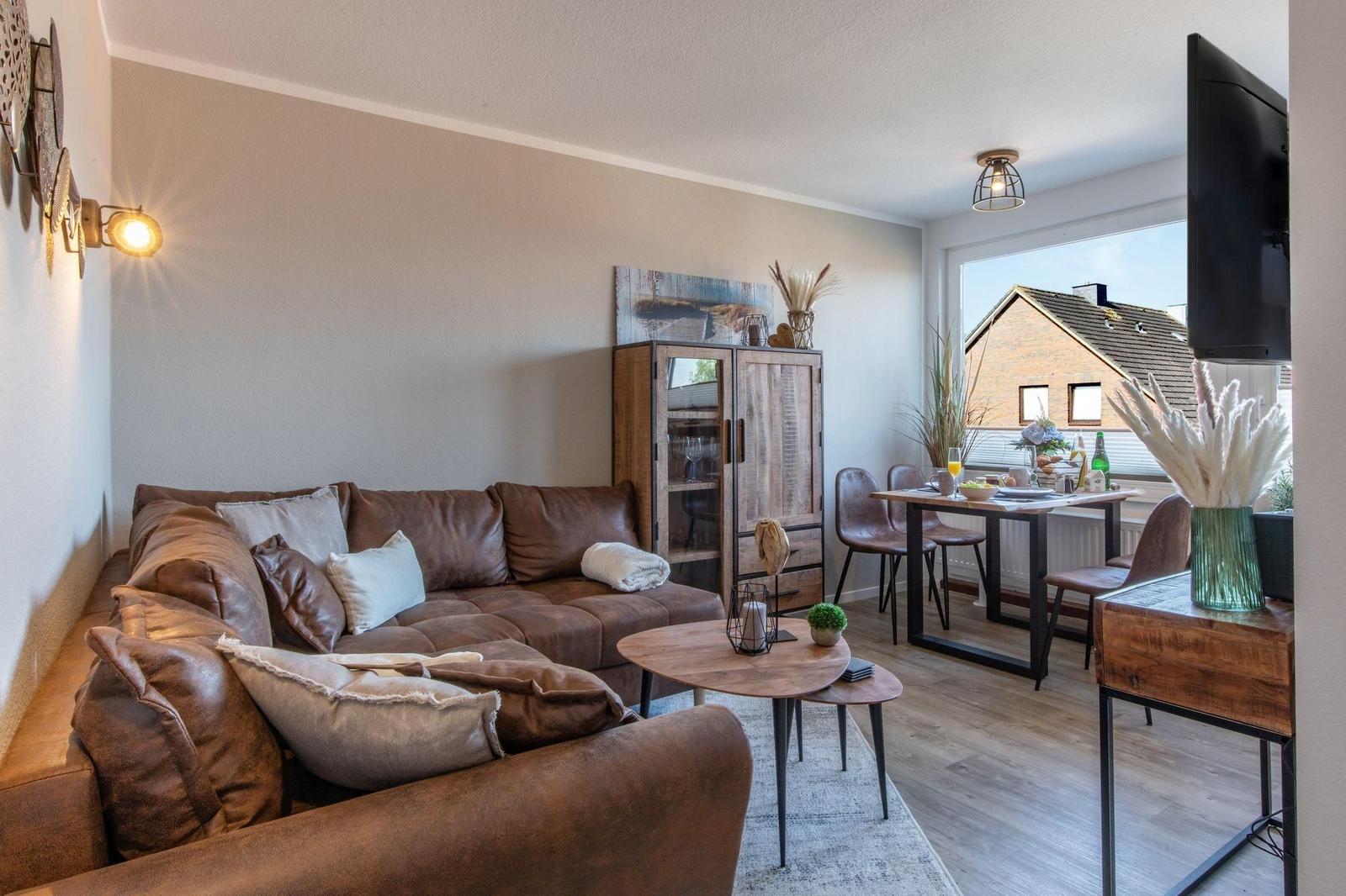 Wohn- und Essbereich mit braunem Sofa, Holztisch und Fernseher.