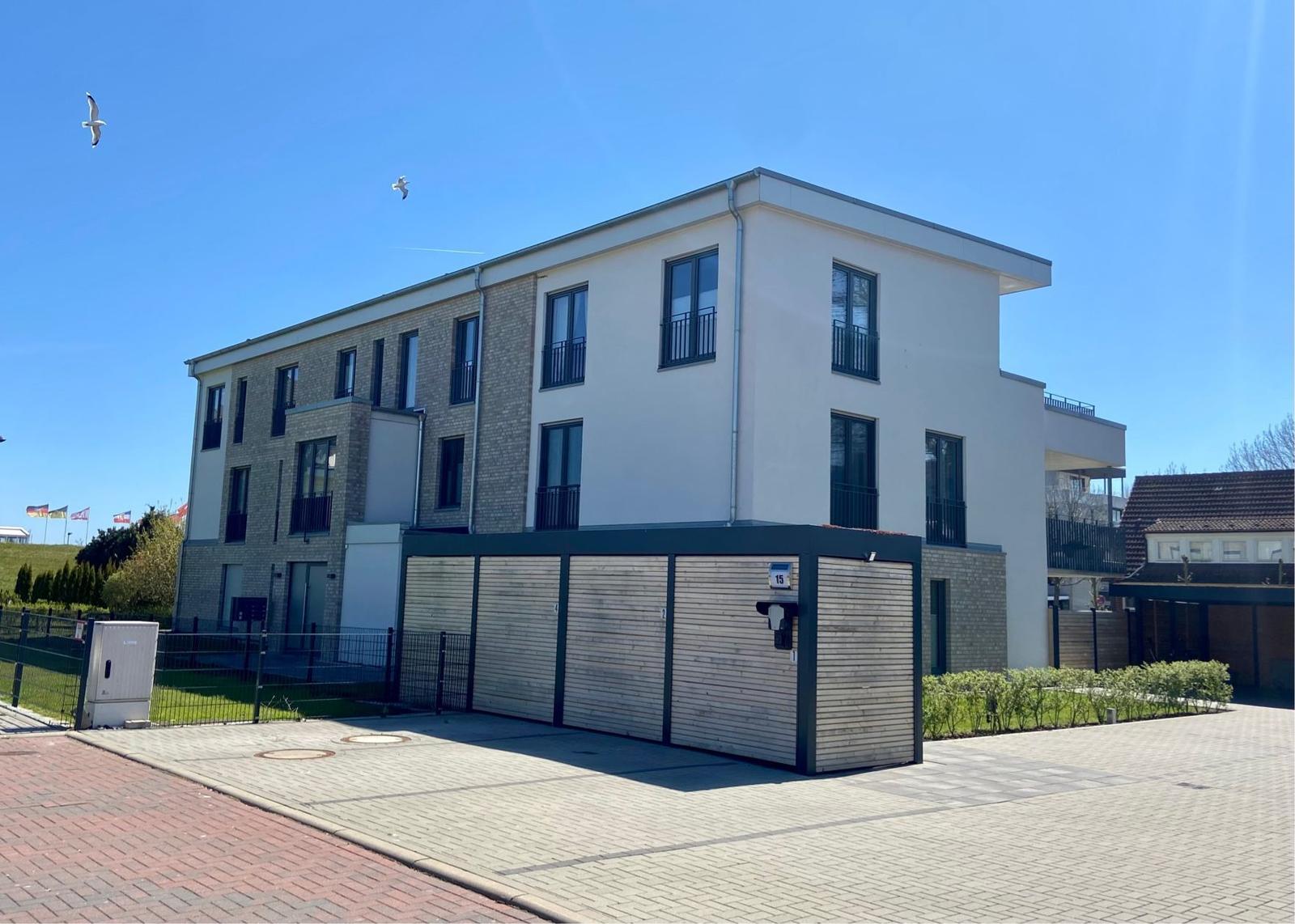 Moderne Wohnung mit Balkon, Garage und Gartenbereich. Helle Fassade und große Fenster.
