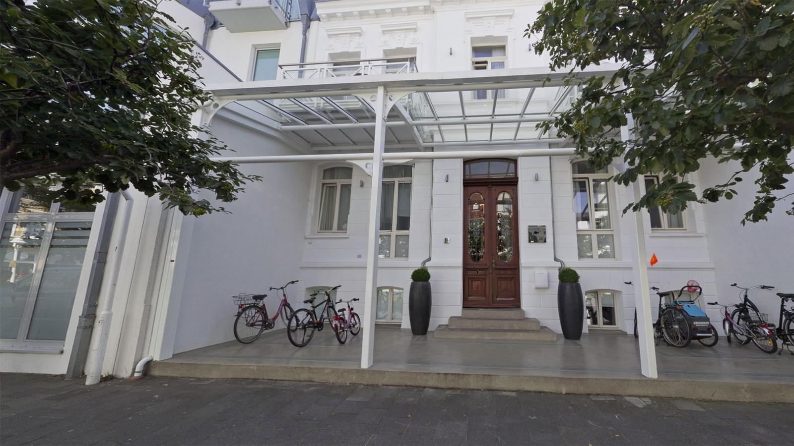 Weiße Fassade mit Eingangstreppe und Fahrrädern vor dem Haus.