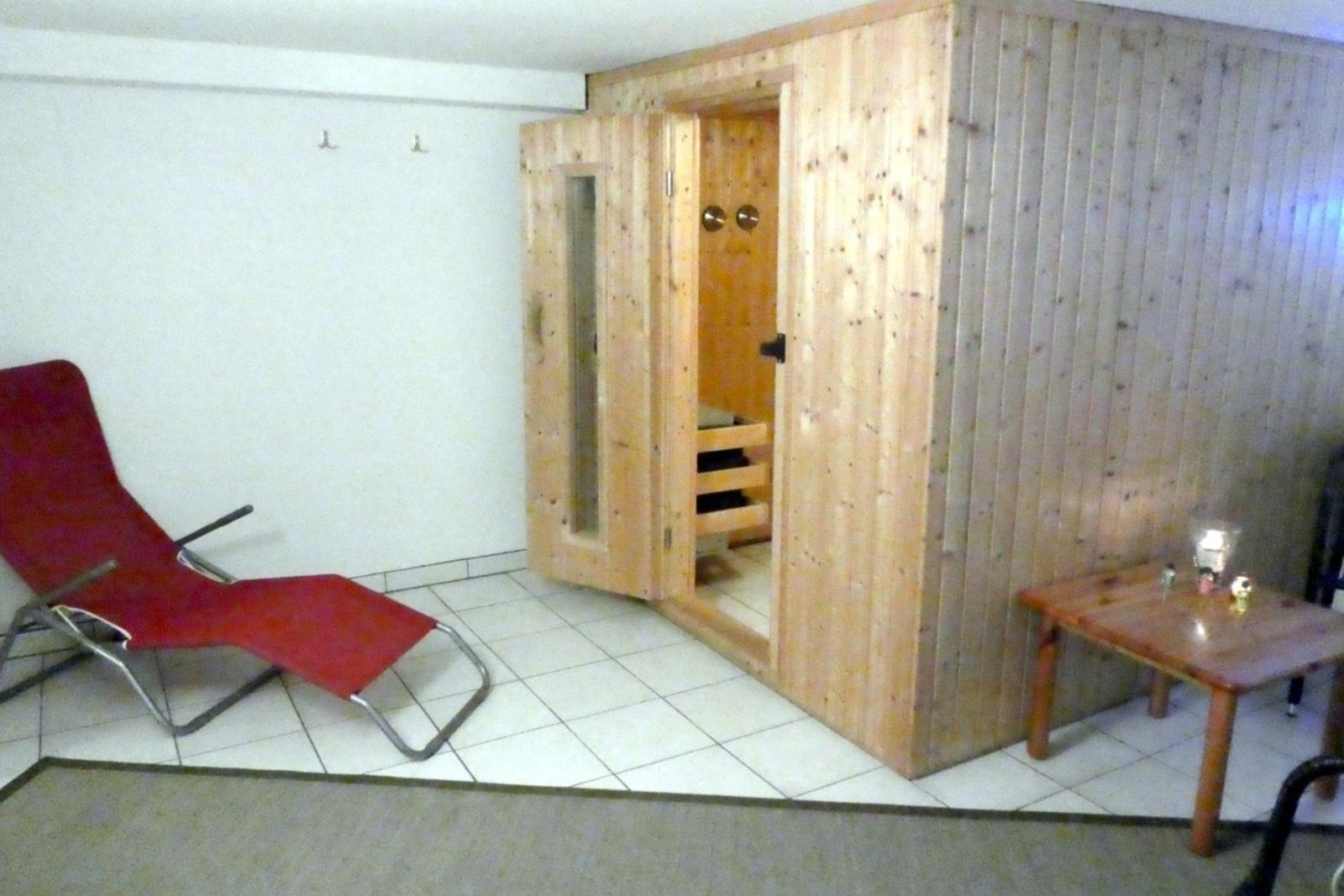 Sauna with wooden walls, red lounge chair, and table with glasses.
