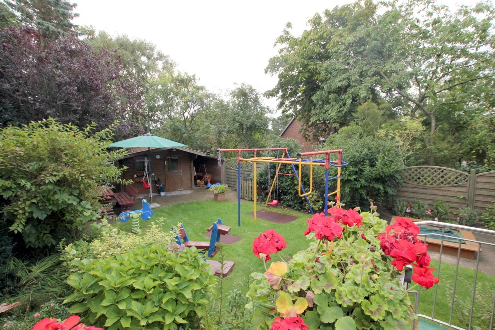 Hinterhof mit Spielplatz, Schaukel, Klettergerüst und Rutsche. Grasfläche und Blumenkästen.