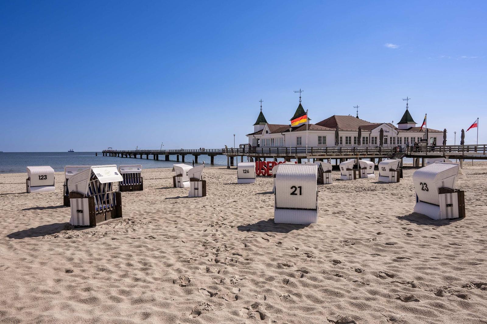 Weißes Gebäude mit rotem Dach auf Steg über Sanddünen und Meer