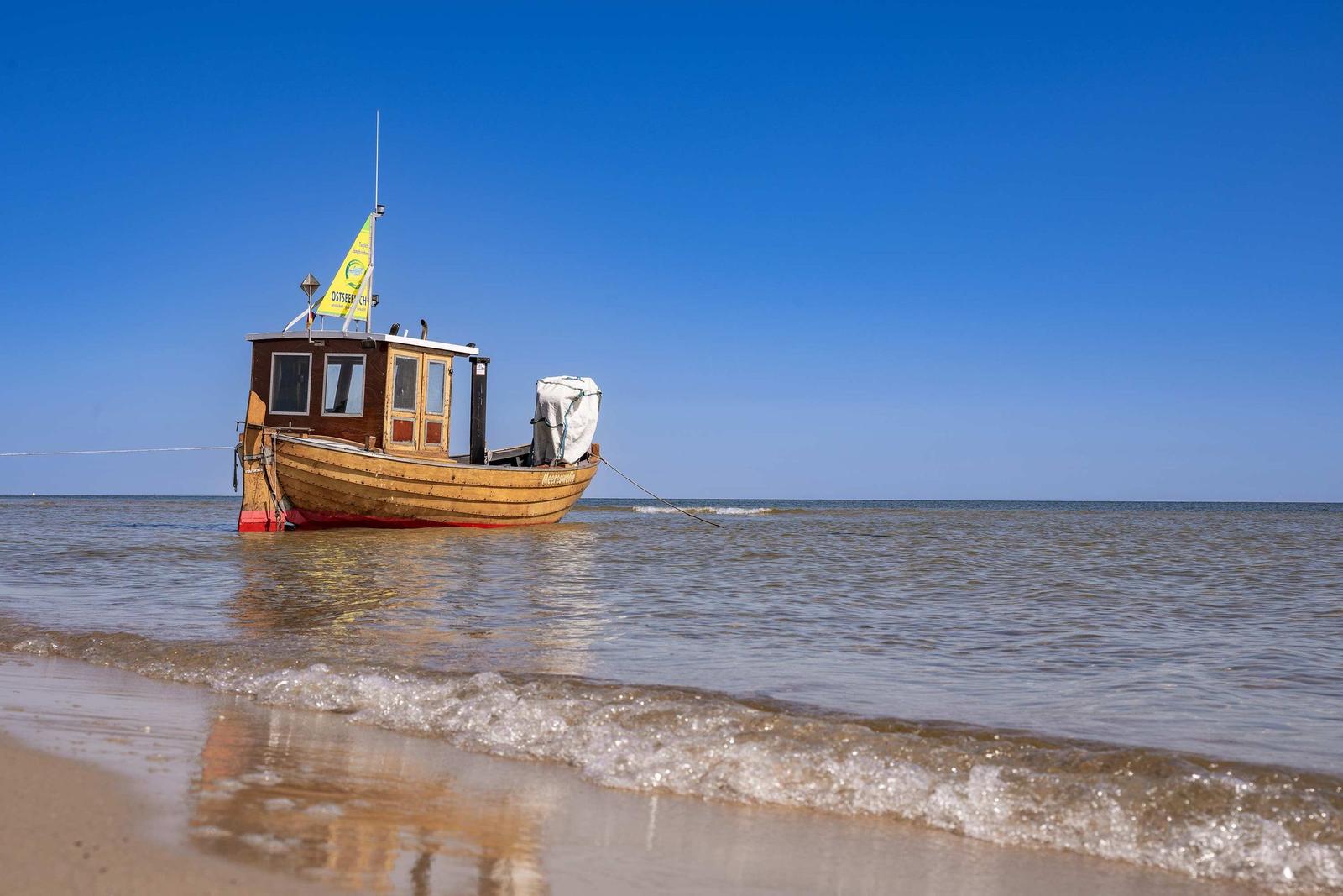 Strand mit Strandkorb und USEDOM-Schild, Hintergrund: weißes Gebäude mit deutscher Flagge.