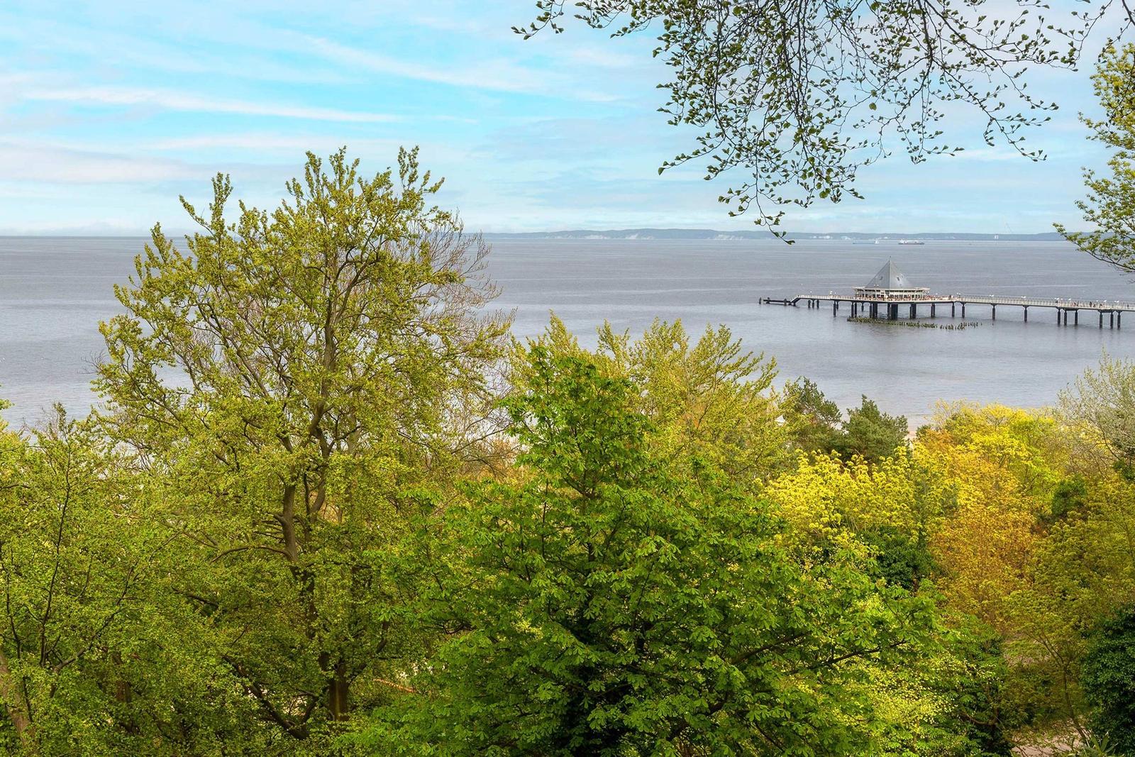 Zwei Personen entspannen sich auf Liegestühlen mit Blick auf See und Pier.