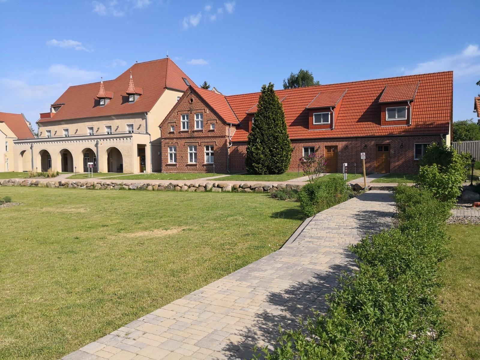 Rotes Backsteingebäude mit weißen Fenstern und Terrasse mit Gartenmöbeln.