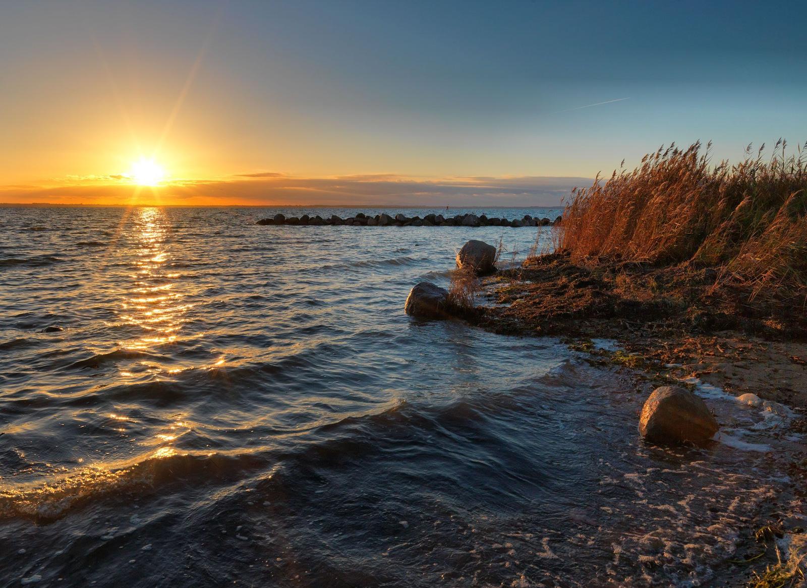 Sonnenuntergang über dem Meer mit Wellen und Steinen an der Küste.