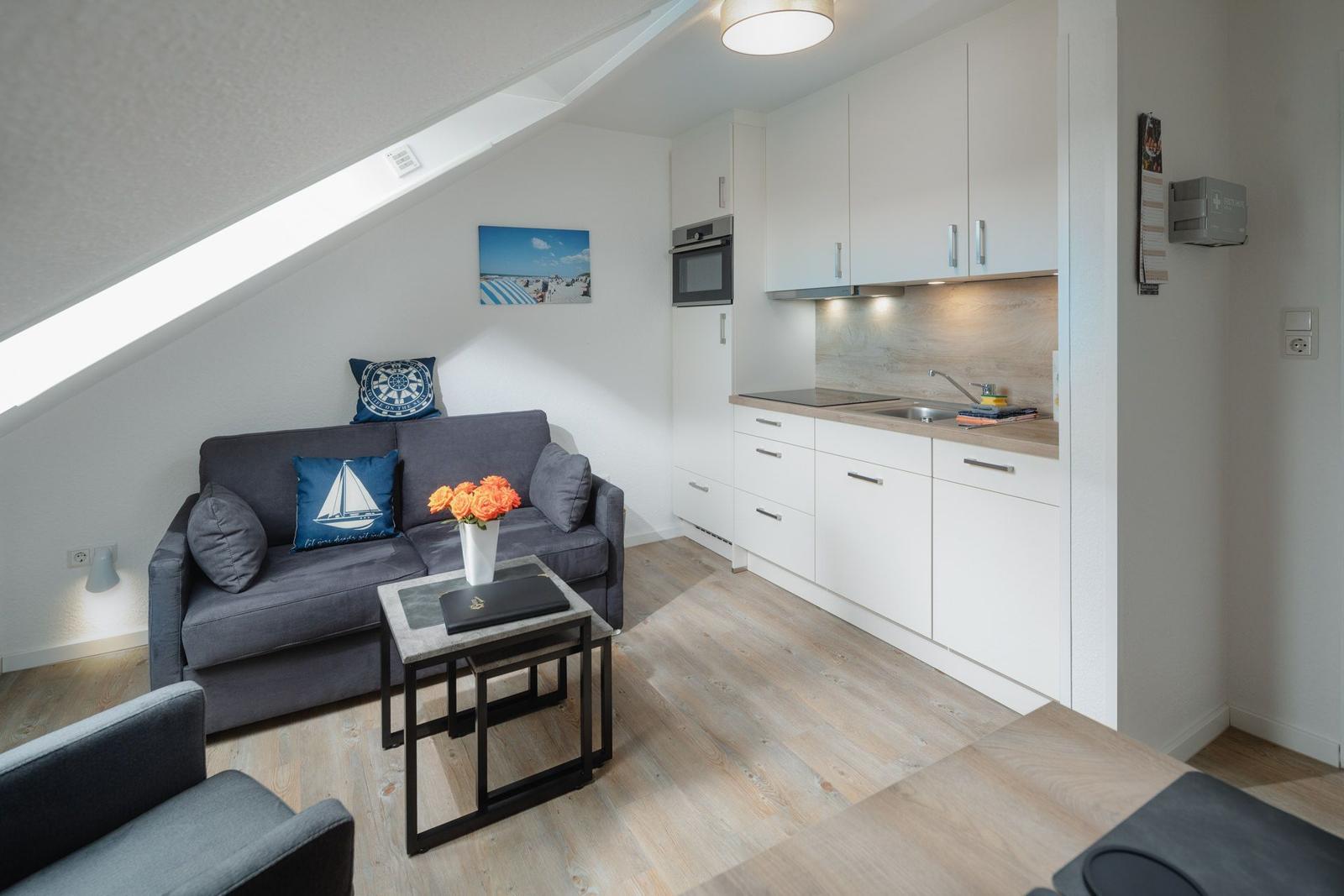 Ein Raum mit Tisch, zwei Stühlen, Fernseher und Sessel unter Dachschrägen mit Dachfenster.