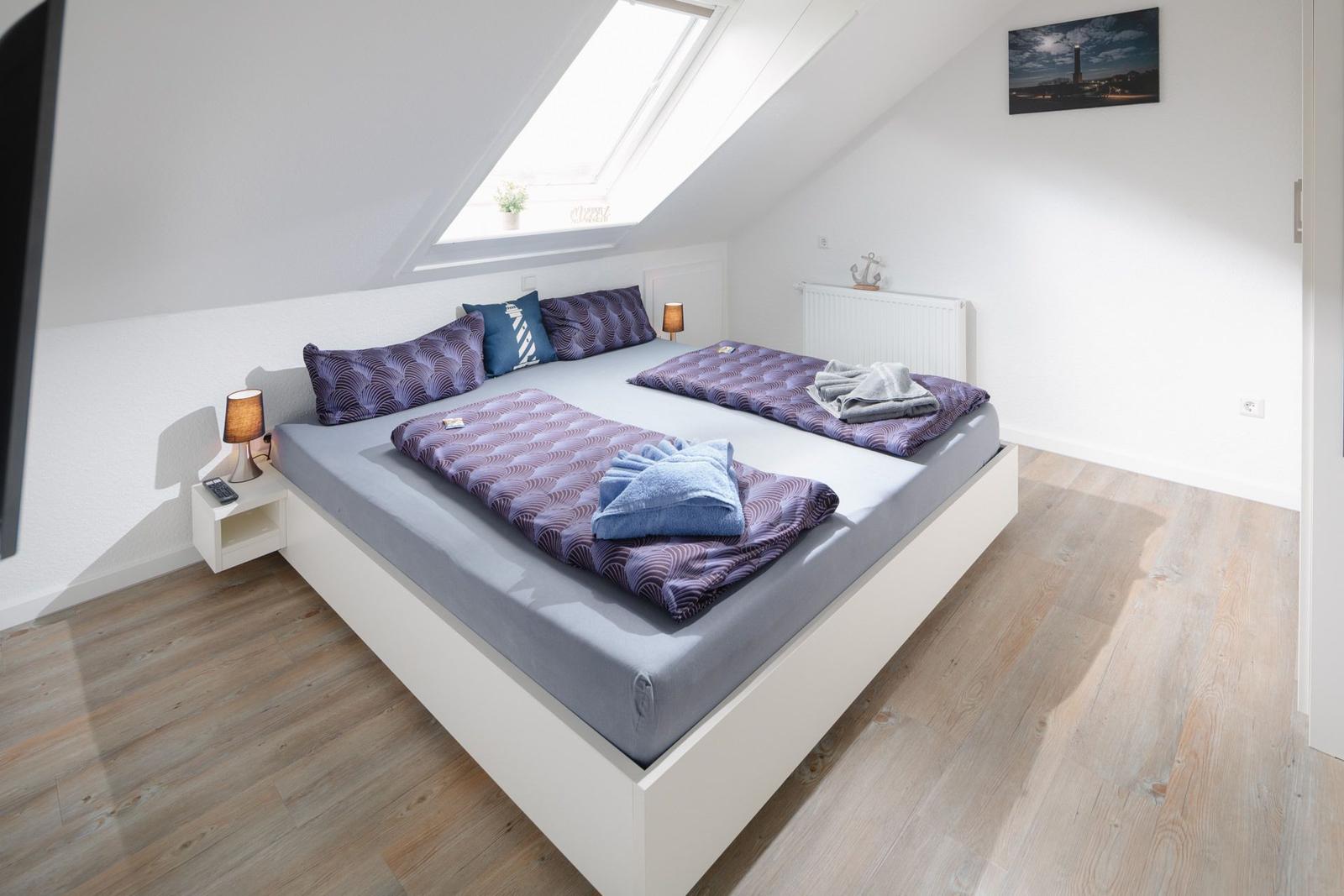 Schlafzimmer mit Dachschräge, Bett, Kleiderschrank und Wandbild.