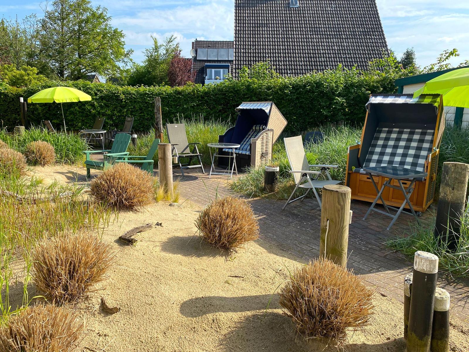 Wohnzimmer mit Sofa, Sessel und Tisch. Wandbild zeigt Strand. Küche im Hintergrund.
