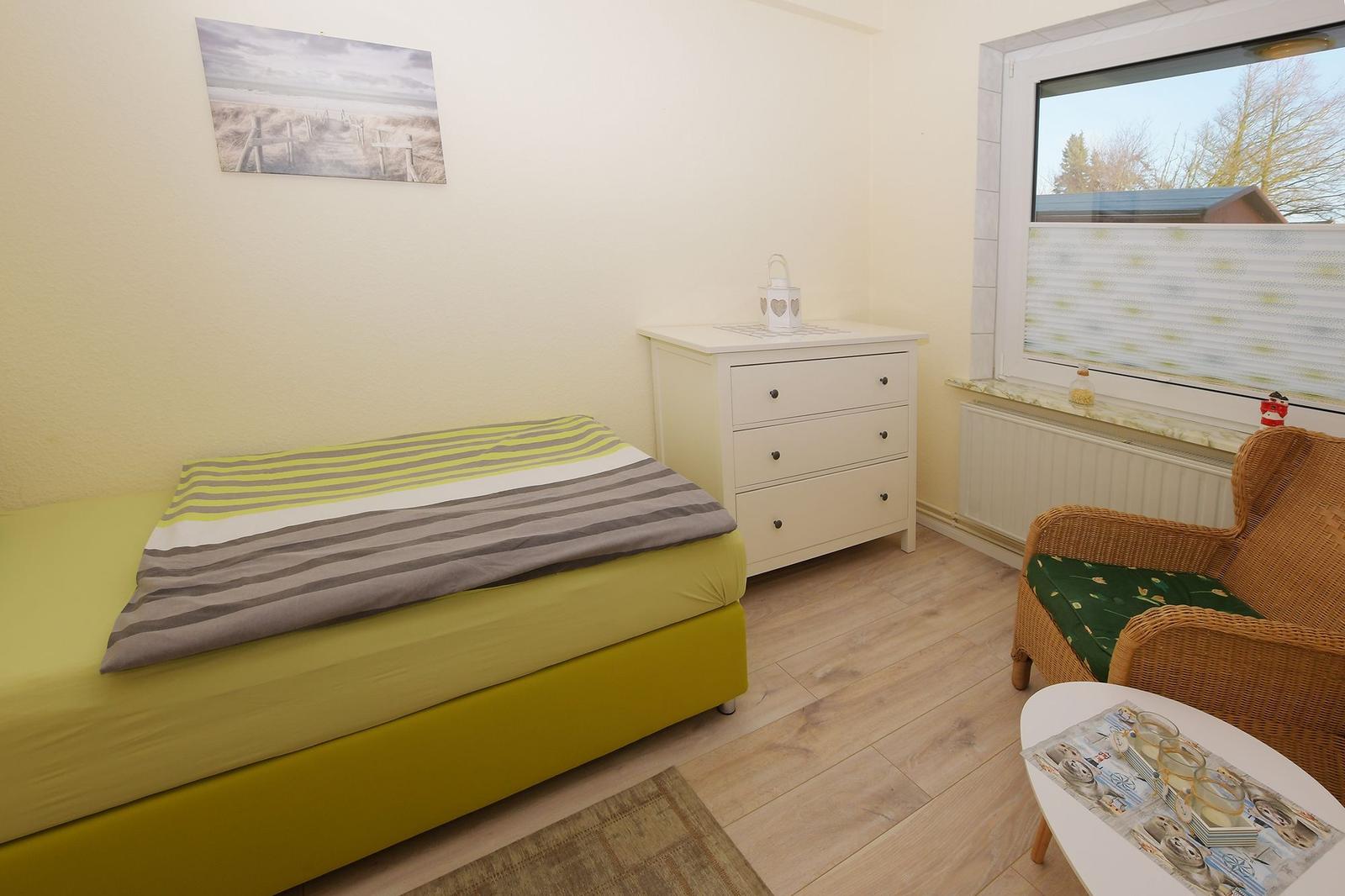 Schlafzimmer mit Doppelbett, Holzschrank und Fenster mit weißen Vorhängen.