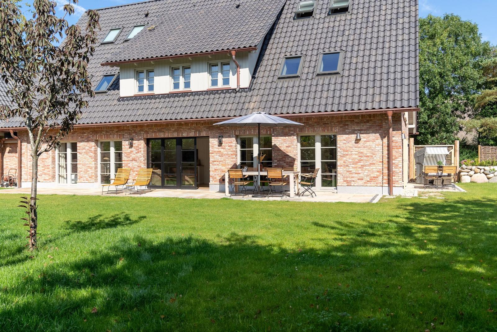 Haus mit Terrasse, Garten und Sitzgelegenheiten unter Sonnenschirm.