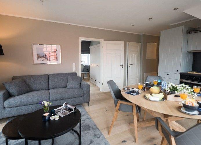 Essbereich mit Tisch und Stühlen, Wohnbereich mit Sofa und Fernseher, große Fenster mit Blick.