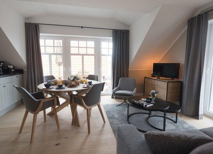 Wohn- und Essbereich mit Sofa, Tisch und Fernseher. Fenster mit Blick auf Balkon.