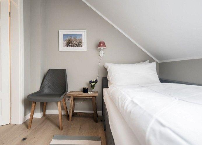 Schlafzimmer mit Dachschräge, Bett, zwei Fenster und Nachttisch mit Lampe.
