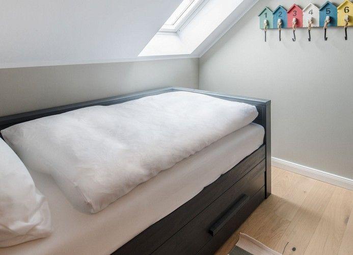 Ein Bett mit Kissen und einer Bettdecke neben einem Nachttisch mit Lampe und Blumen.