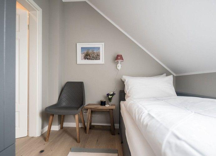 Schlafzimmer mit Bett, Stuhl und Kleiderschrank unter Dachschrägen.
