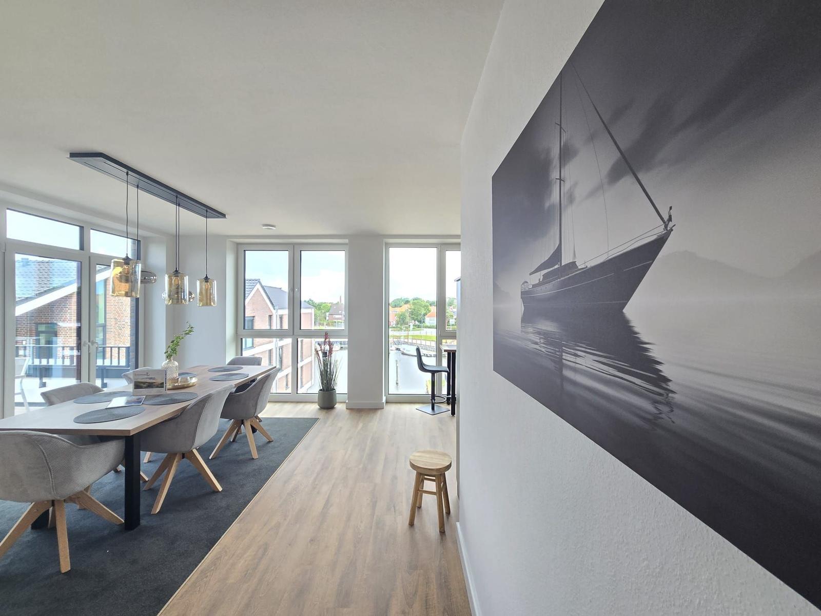 Esszimmer mit Holztisch, grauen Stühlen und großem Fensterblick auf Balkon und Umgebung.