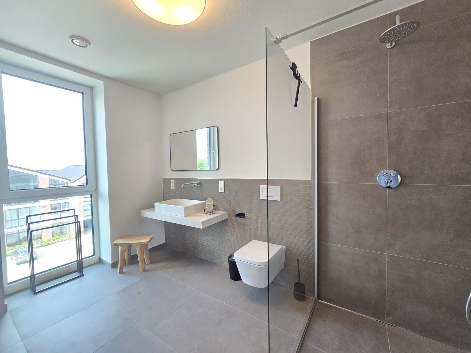 Badezimmer mit WC, Waschbecken und Spiegel. Wandfliesen und Handlauf.