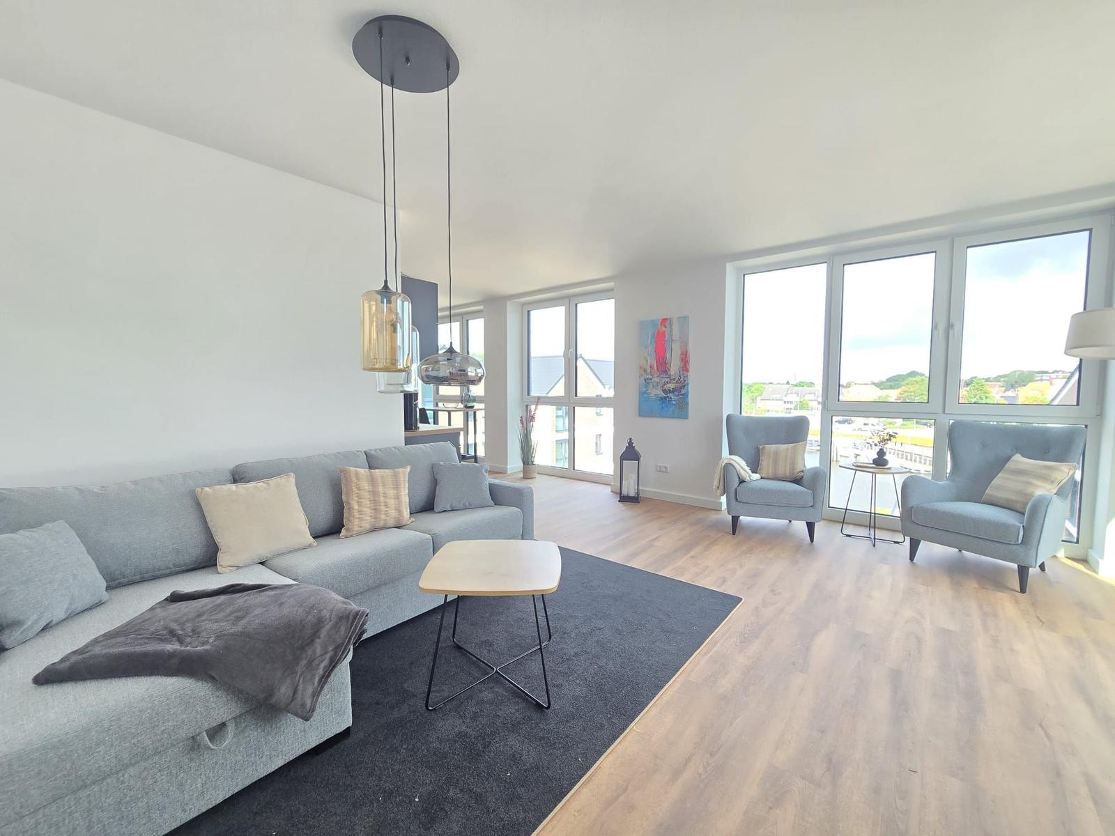 Wohnzimmer mit Sofa, Sesseln, Fernseher und Balkonzugang.