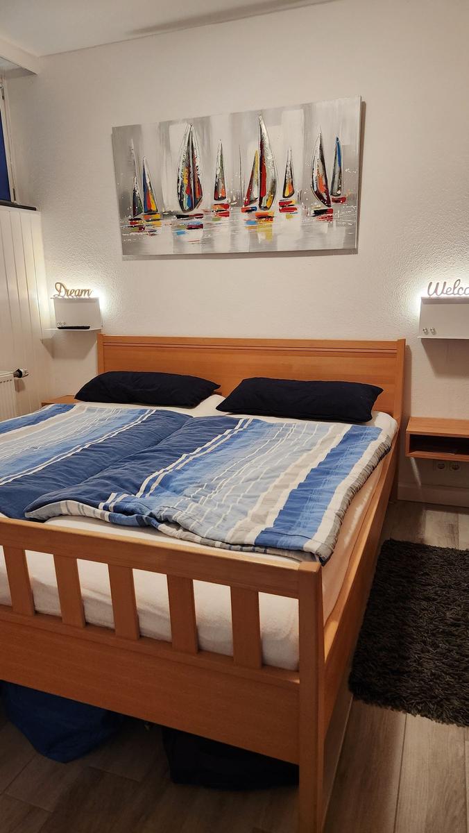 Schlafzimmer mit Bett, Kleiderschrank und Wandlampe mit Welcome-Schild.