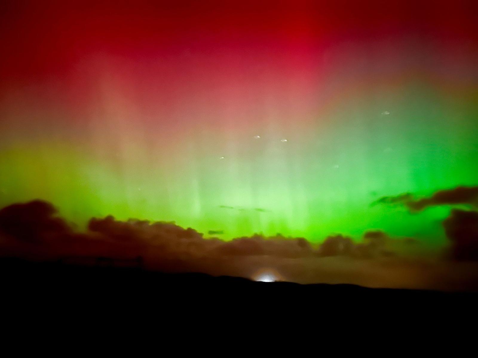 Rot- und grüne Nordlichter über dunklem Himmel mit Wolken.