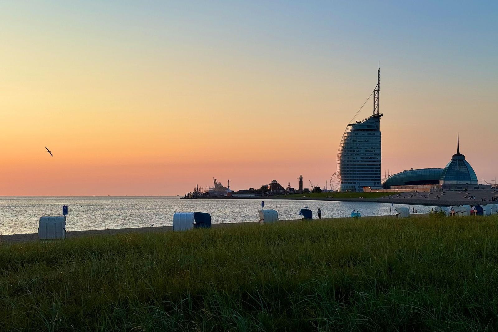 Roter Leuchtturm am Wasser mit Boot und Steinanlagen im Vordergrund.
