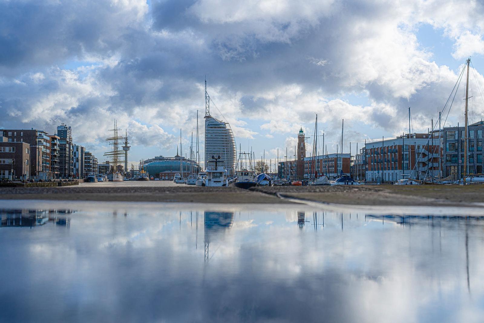 Hafen mit Containerkränen und Schiffen im Wasser unter blauem Himmel.