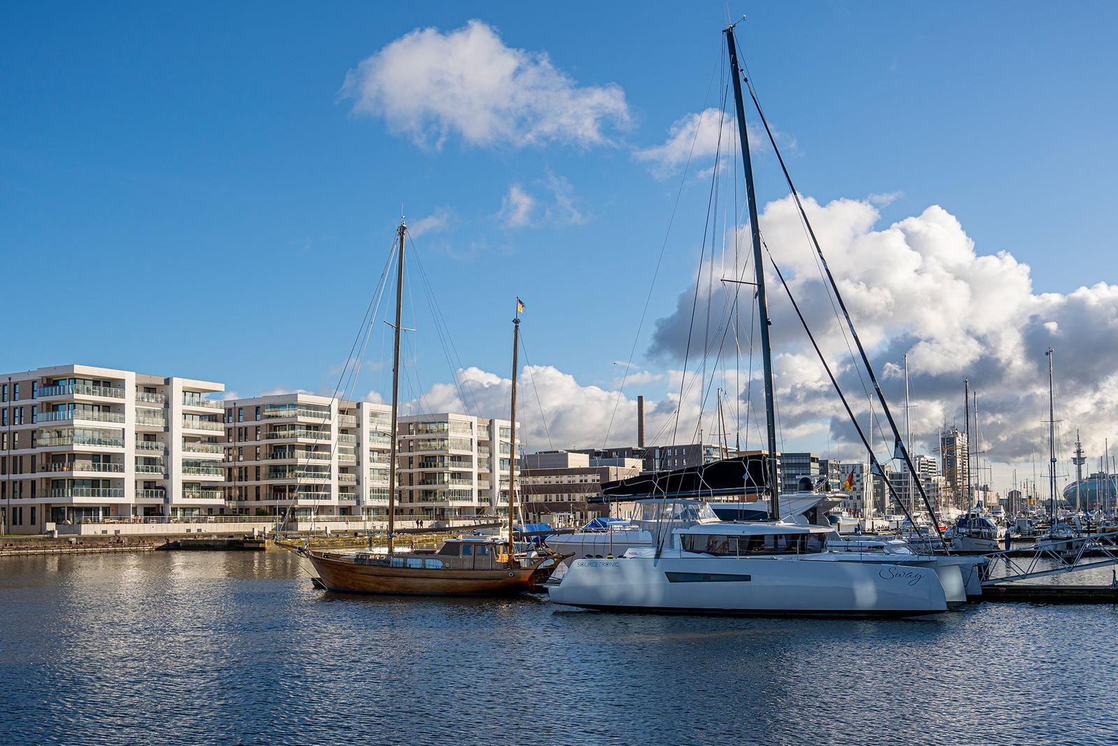 Hafen mit Booten und modernen Gebäuden unter bewölktem Himmel.