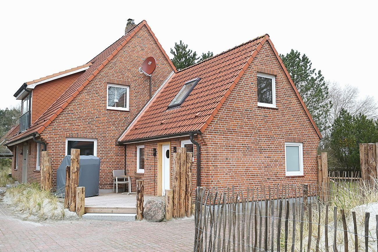 Rotes Ziegelhaus mit Dachterrasse und Holzgeländer. Eingangstür und Fenster sind sichtbar.